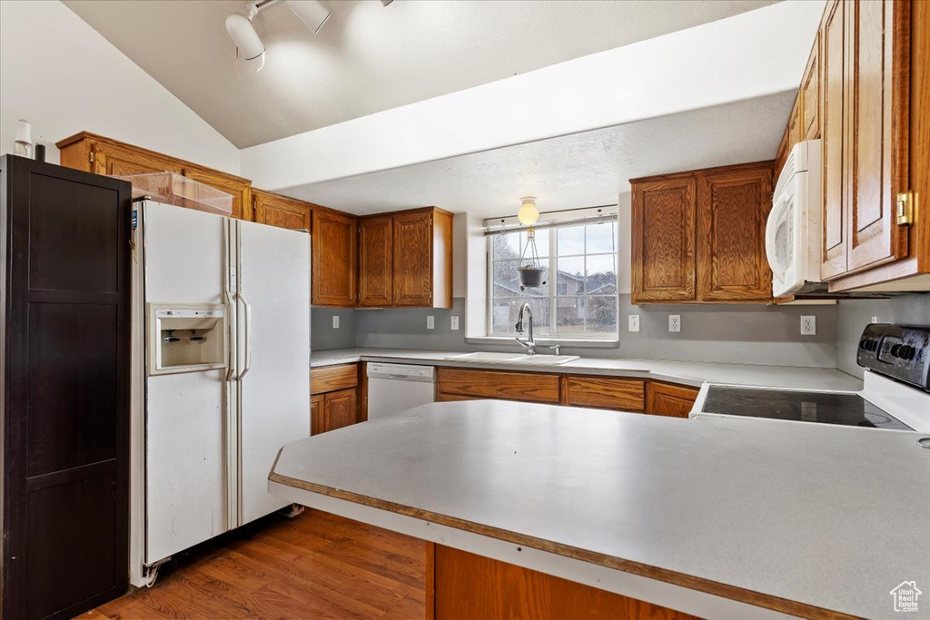 Kitchen with white appliances, a peninsula, brown cabinets, wood finished floors, and vaulted ceiling