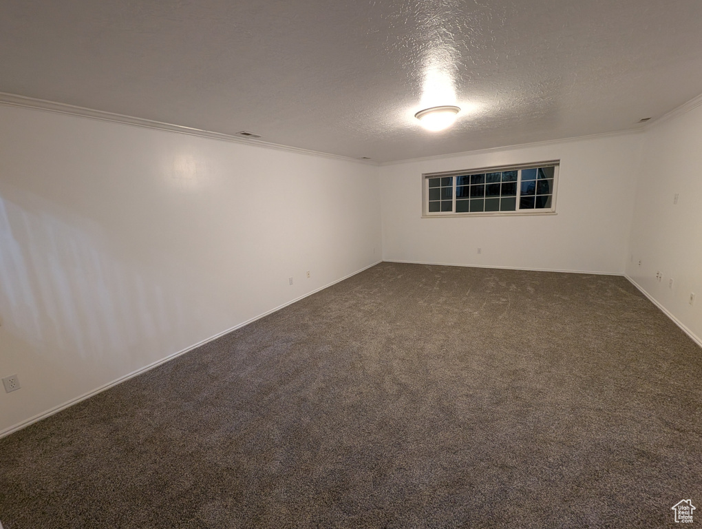 Empty room with ornamental molding, dark carpet, and a textured ceiling