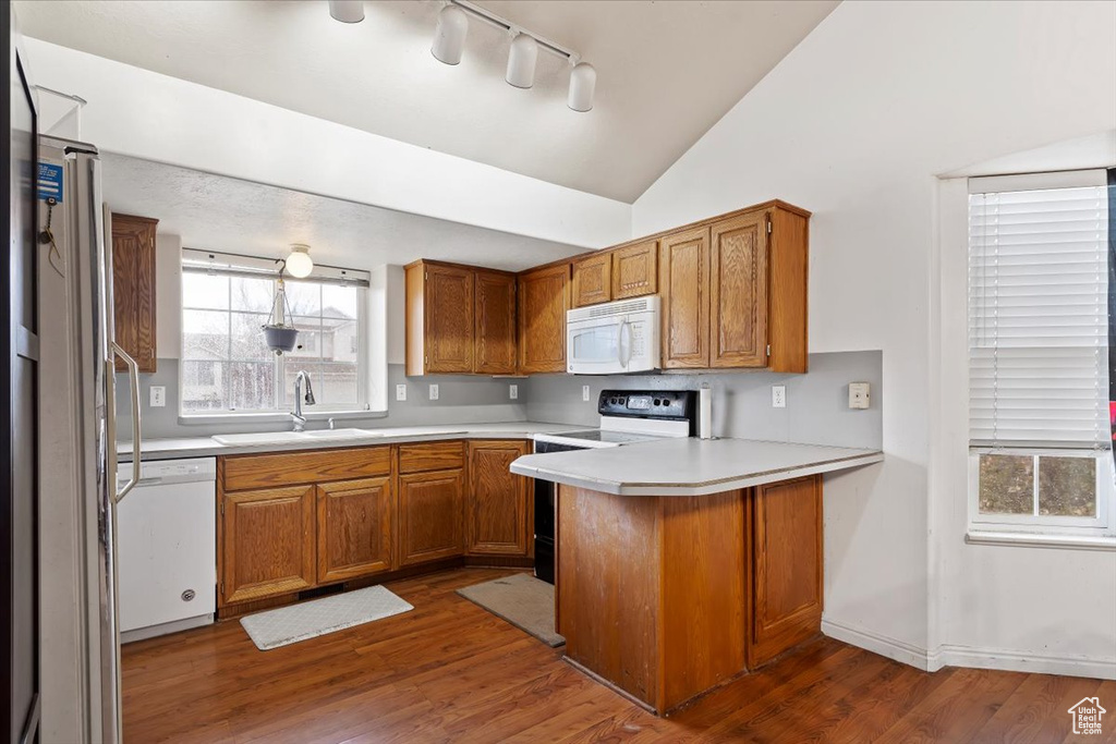 Kitchen featuring white appliances, a peninsula, brown cabinetry, light countertops, and vaulted ceiling