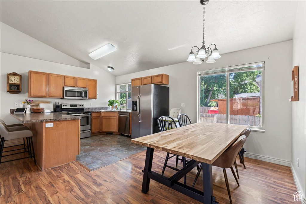 Kitchen featuring stainless steel appliances, a peninsula, vaulted ceiling, a chandelier, and brown cabinetry