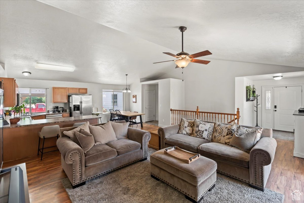 Living area featuring vaulted ceiling, wood finished floors, a ceiling fan, and a textured ceiling