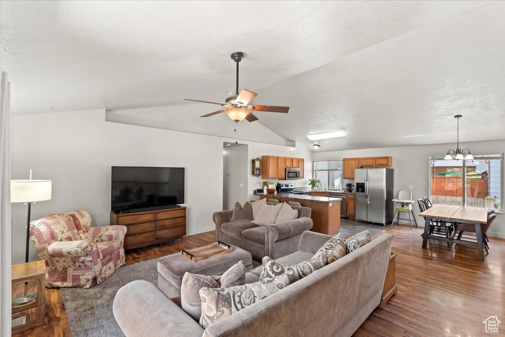 Living area featuring a chandelier, vaulted ceiling, a ceiling fan, and dark wood-style floors