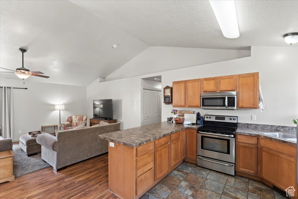 Kitchen with appliances with stainless steel finishes, open floor plan, a peninsula, lofted ceiling, and dark countertops