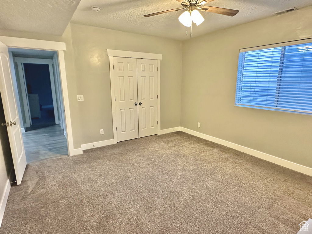 Unfurnished bedroom featuring a textured ceiling, carpet, a closet, and a ceiling fan