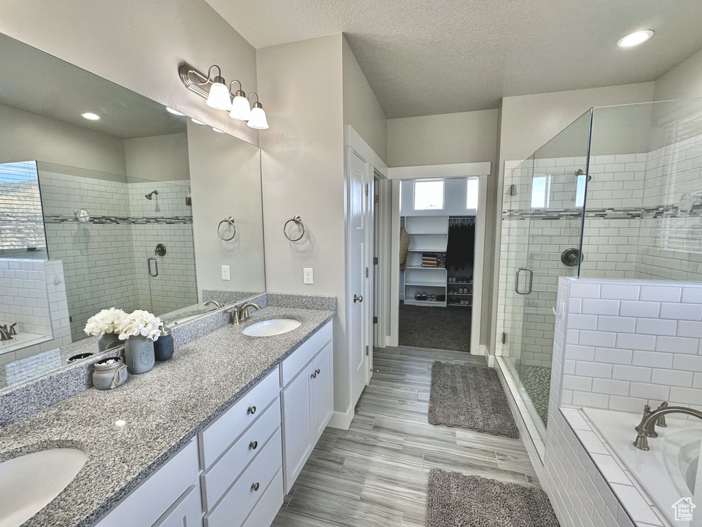 Bathroom with double vanity, a shower stall, a bath, and a textured ceiling