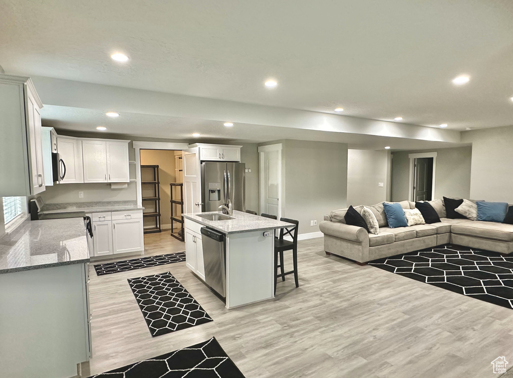 Kitchen with stainless steel appliances, open floor plan, light wood-style floors, recessed lighting, and white cabinets