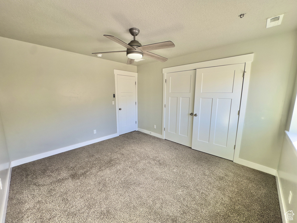 Unfurnished bedroom featuring carpet floors, a textured ceiling, a closet, and a ceiling fan