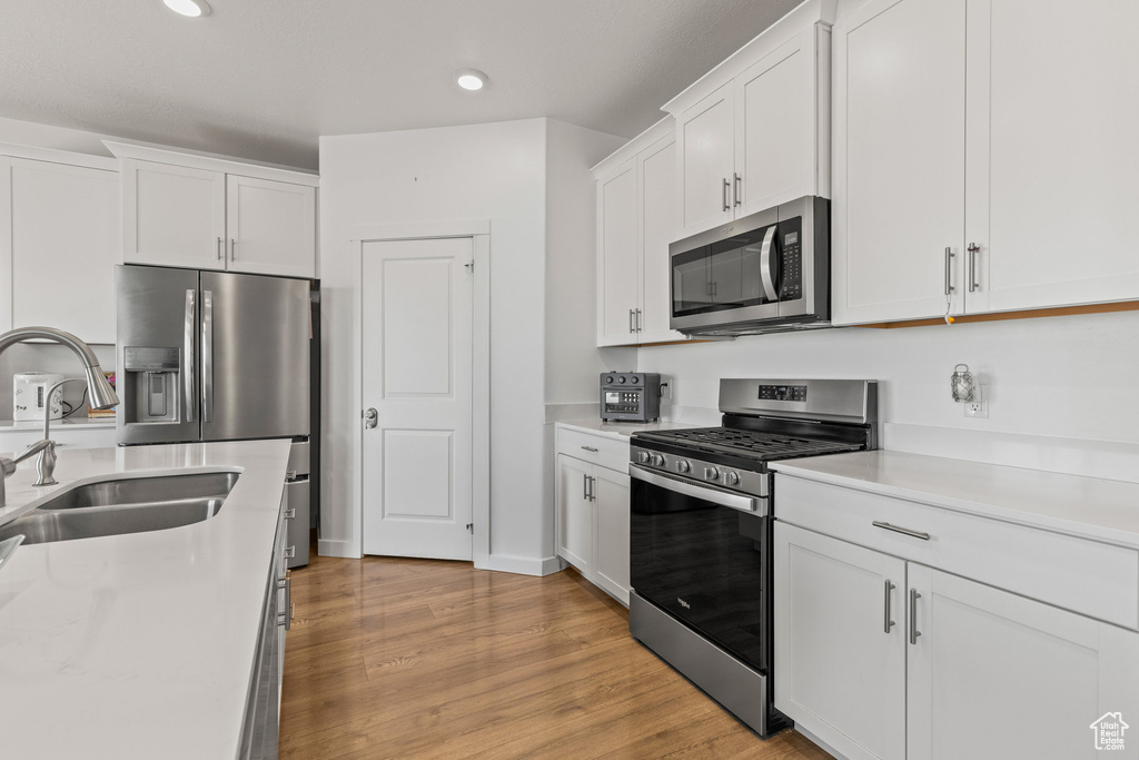 Kitchen featuring stainless steel appliances, white cabinets, light countertops, recessed lighting, and light wood-style flooring