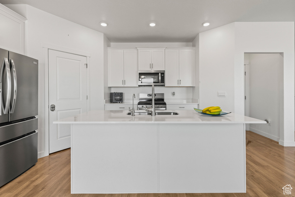 Kitchen with stainless steel appliances, white cabinets, light countertops, light wood-style flooring, and recessed lighting