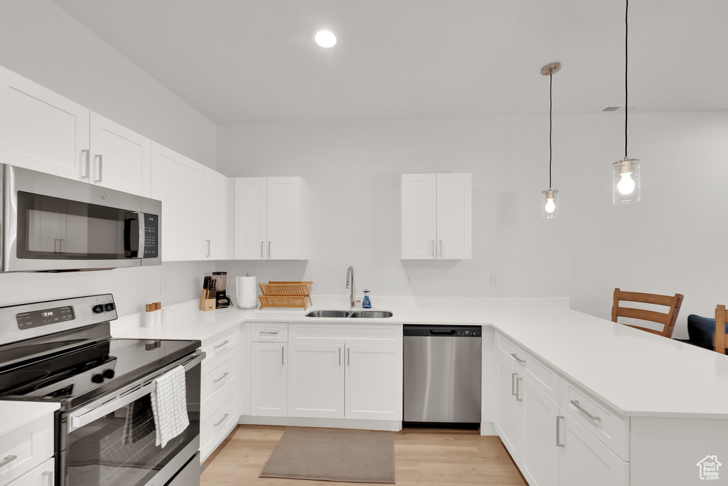 Kitchen with stainless steel appliances, a peninsula, light wood-type flooring, light countertops, and recessed lighting