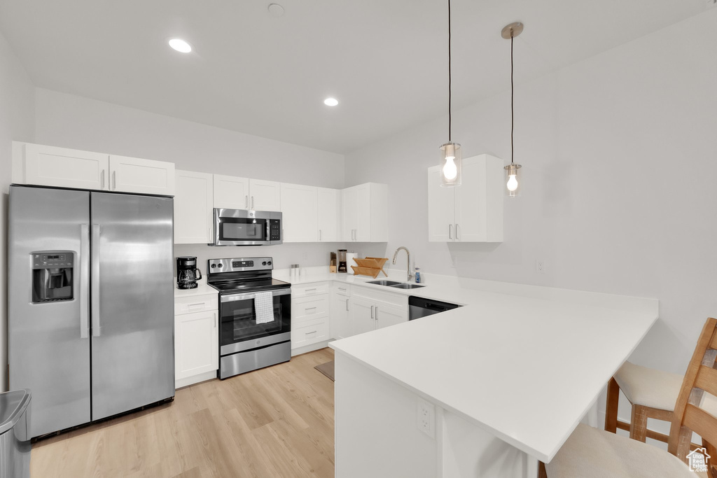 Kitchen featuring appliances with stainless steel finishes, a peninsula, light countertops, light wood-style floors, and a kitchen bar