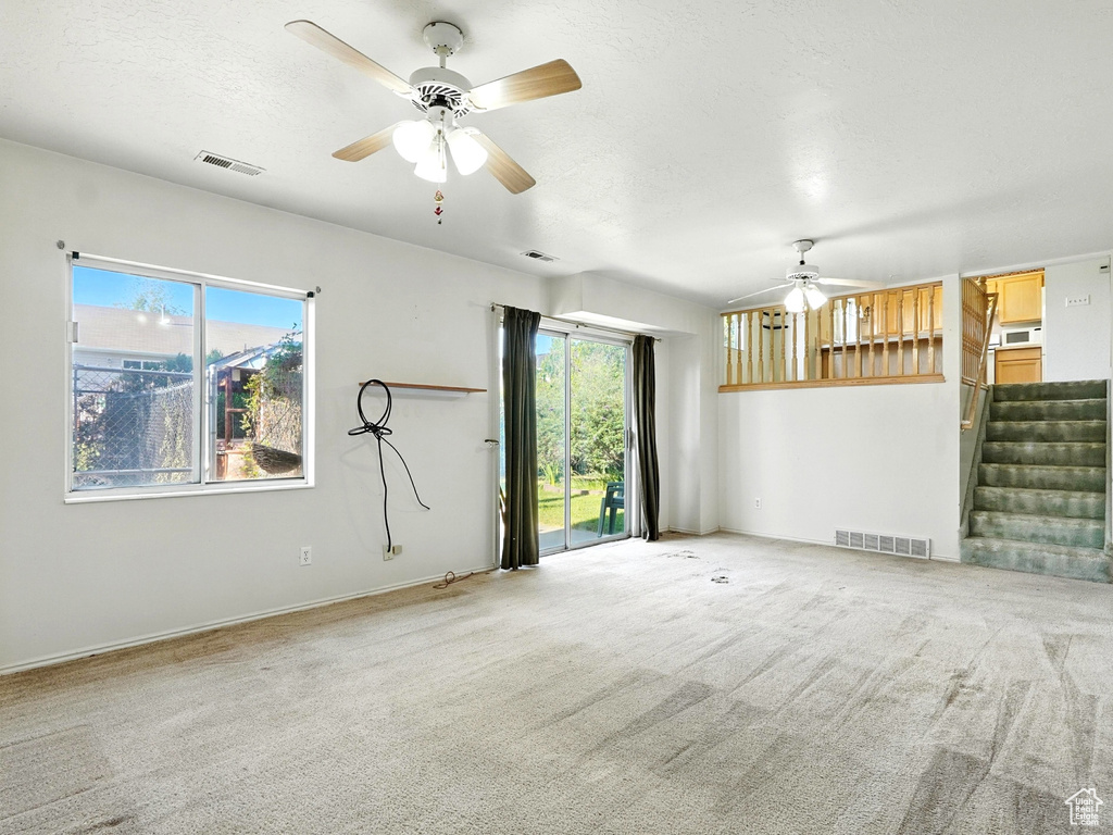 Unfurnished living room featuring ceiling fan, stairway, carpet, and a textured ceiling