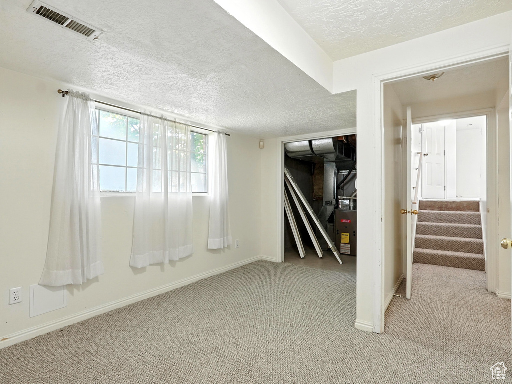 Below grade area with a textured ceiling, light carpet, and stairs