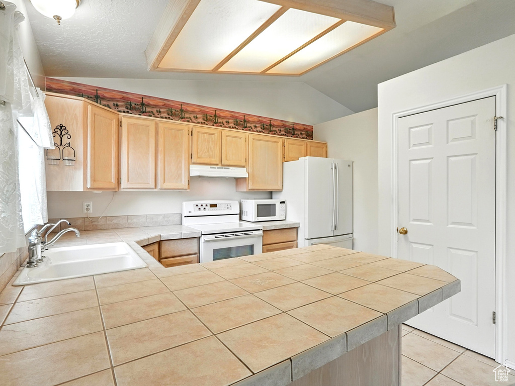 Kitchen with white appliances, light brown cabinetry, under cabinet range hood, vaulted ceiling, and a peninsula