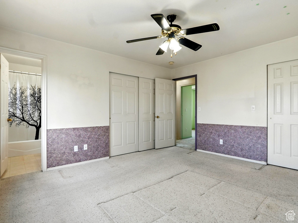 Unfurnished bedroom with a wainscoted wall, ensuite bathroom, and a ceiling fan