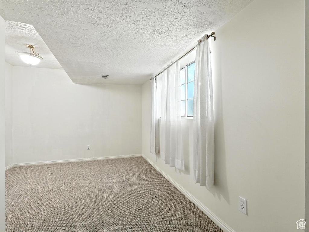 Carpeted spare room with a textured ceiling and baseboards