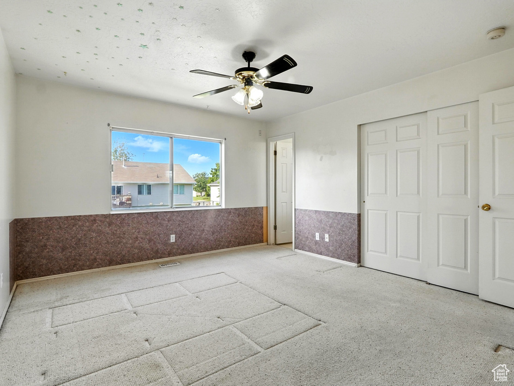 Unfurnished bedroom featuring a wainscoted wall, a ceiling fan, and a closet