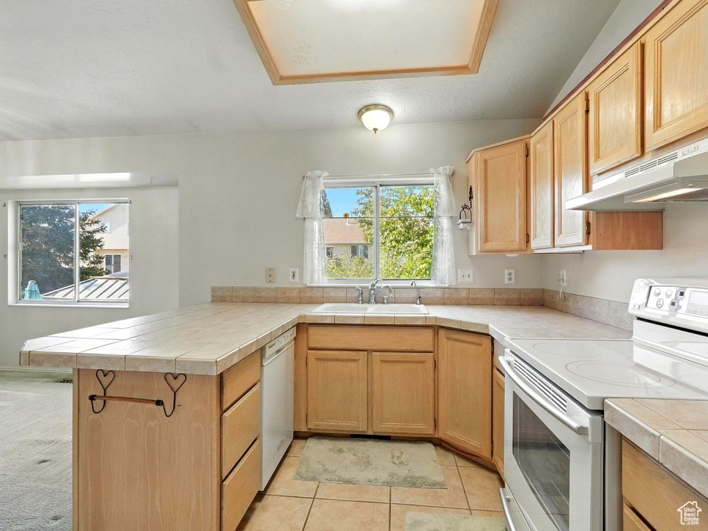 Kitchen featuring white appliances, under cabinet range hood, a peninsula, tile countertops, and light tile patterned flooring