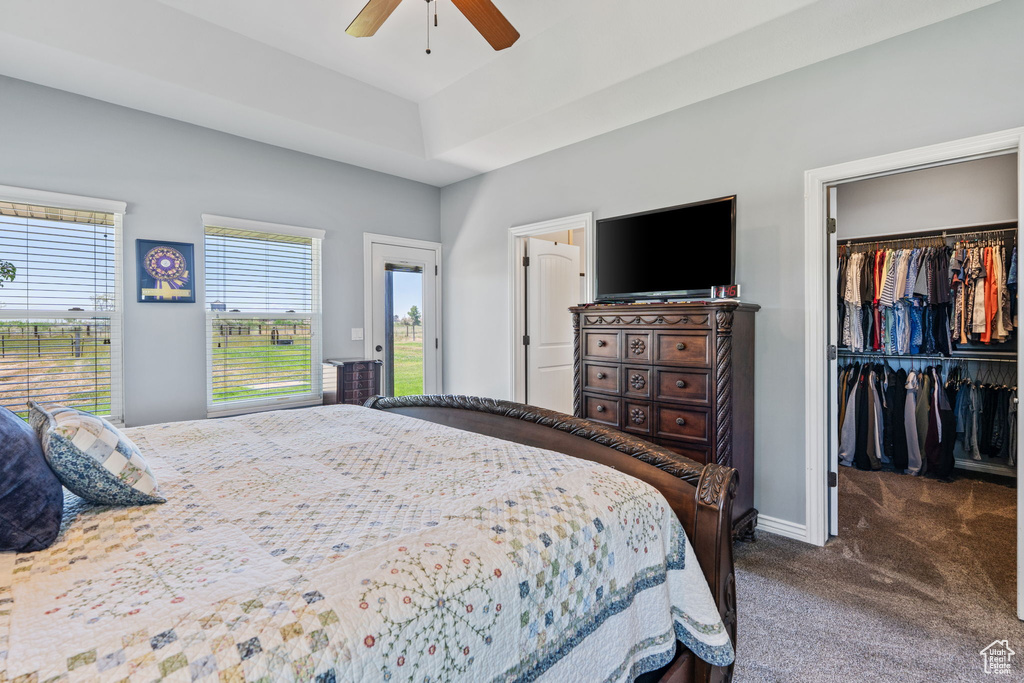 Bedroom with dark carpet, a spacious closet, a closet, ceiling fan, and access to exterior