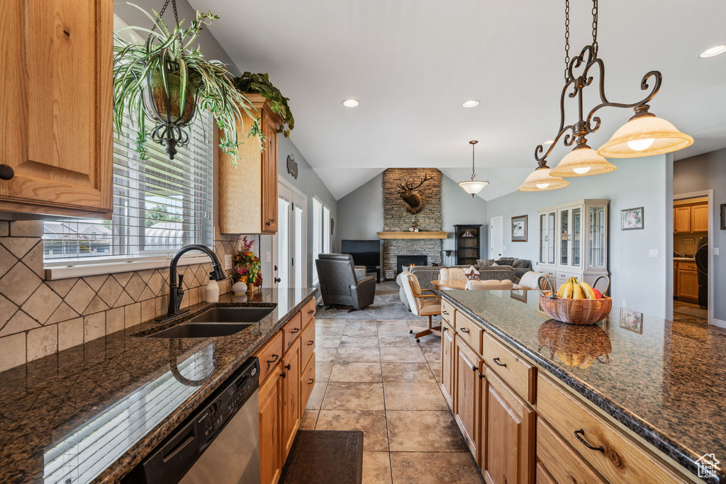 Kitchen featuring lofted ceiling, a stone fireplace, backsplash, dark stone counters, and open floor plan