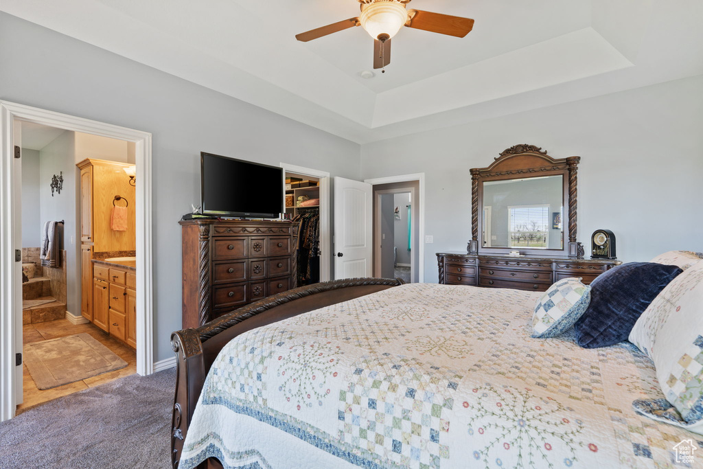 Carpeted bedroom featuring a walk in closet, a raised ceiling, a closet, ensuite bath, and ceiling fan
