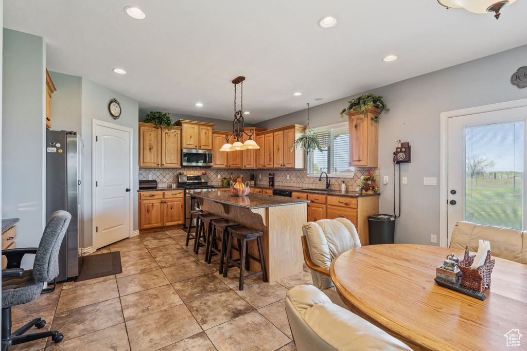 Kitchen with appliances with stainless steel finishes, dark countertops, a kitchen bar, tasteful backsplash, and a kitchen island