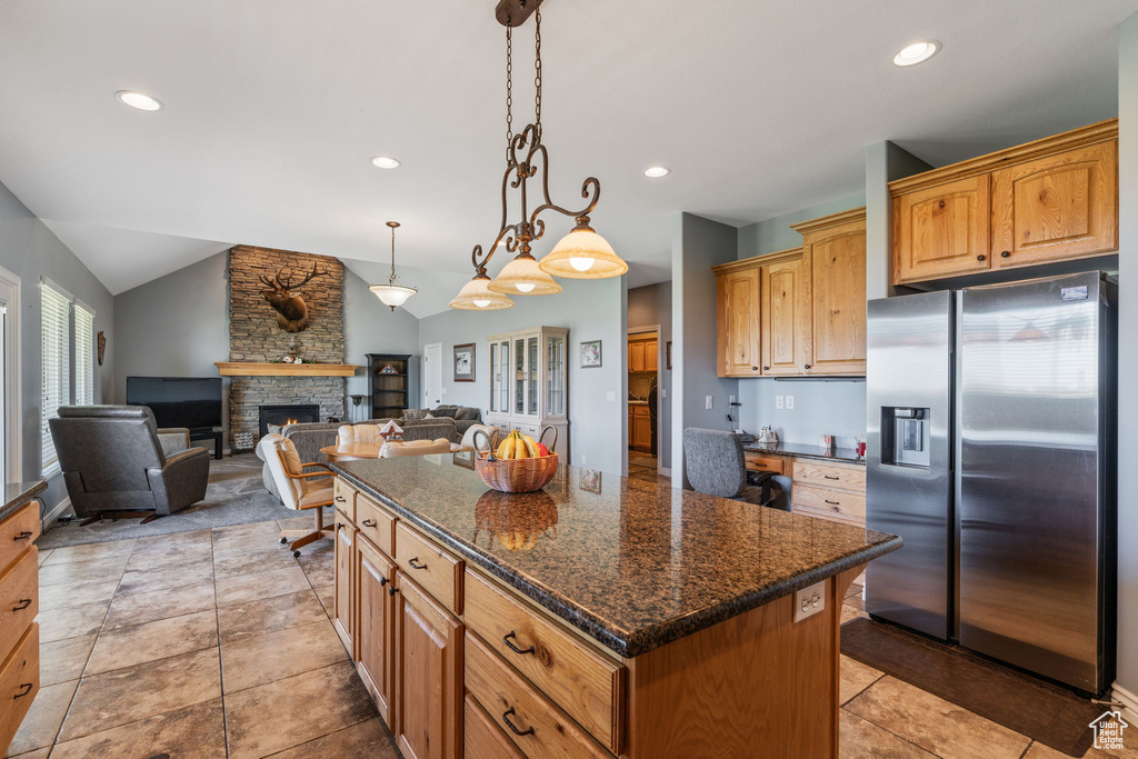 Kitchen featuring stainless steel fridge with ice dispenser, vaulted ceiling, a center island, a fireplace, and pendant lighting