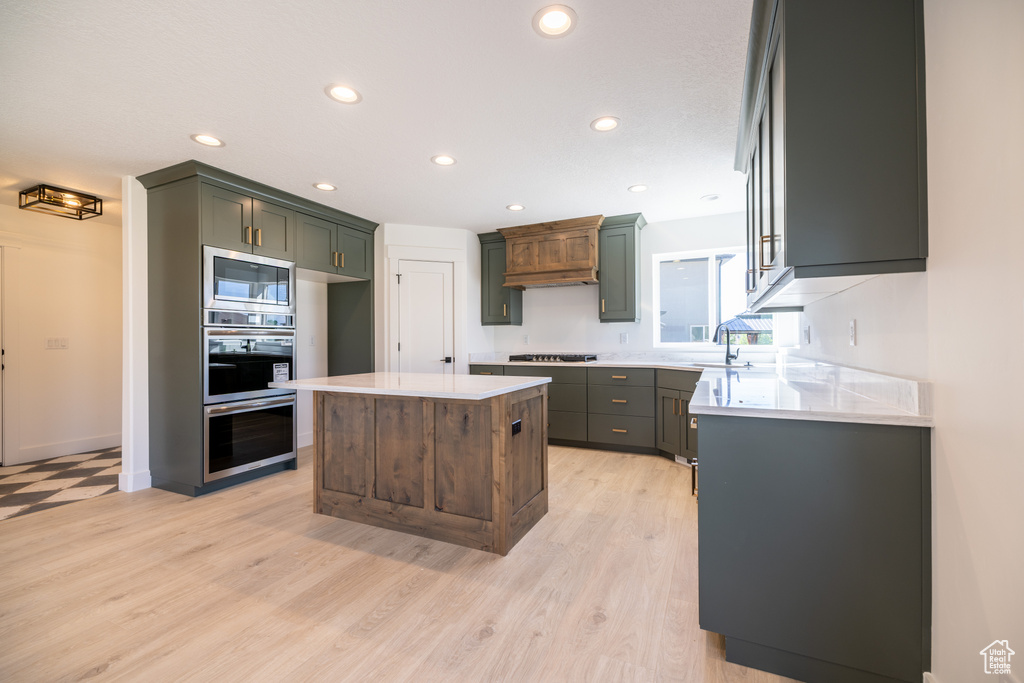 Kitchen with stainless steel appliances, light countertops, recessed lighting, light wood-type flooring, and a center island