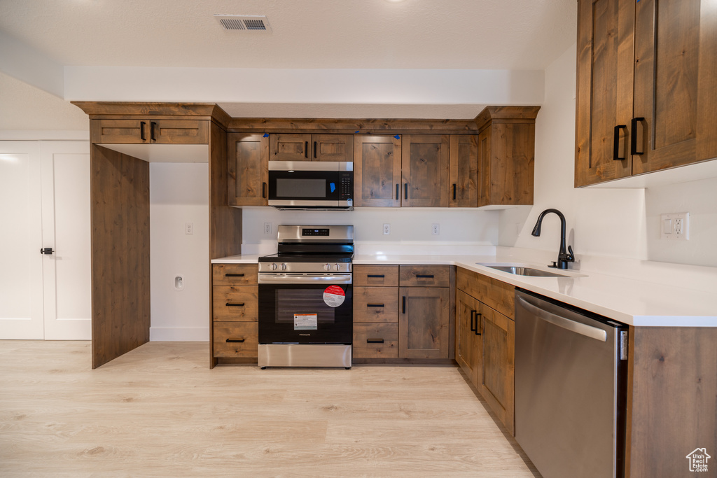 Kitchen with appliances with stainless steel finishes, light wood finished floors, and light countertops
