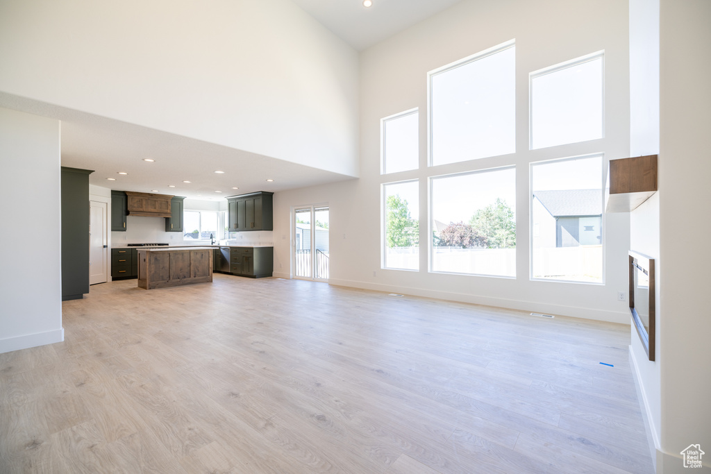 Unfurnished living room featuring light wood finished floors, recessed lighting, and a towering ceiling