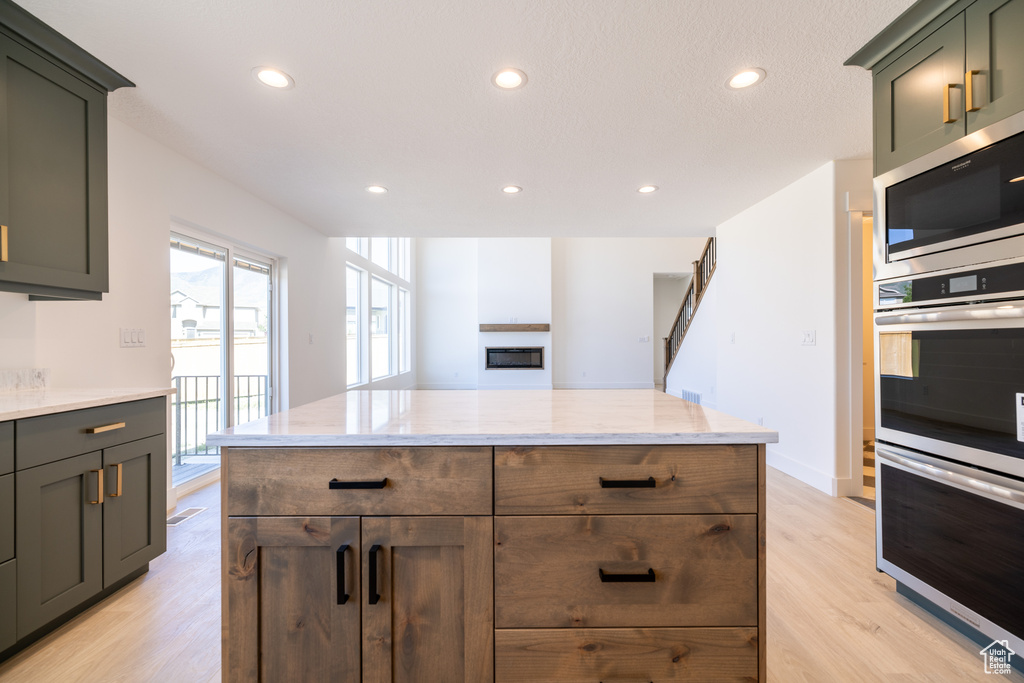 Kitchen with stainless steel appliances, light wood-style floors, recessed lighting, light stone countertops, and a fireplace