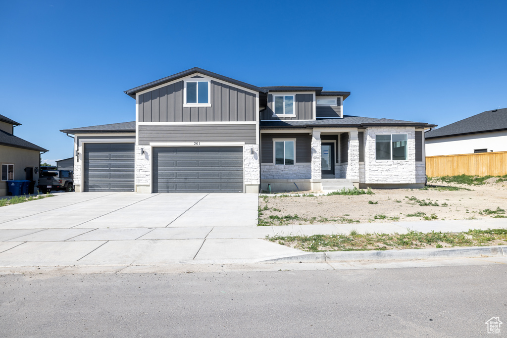 View of front facade with a garage, driveway, stone siding, a porch, and board and batten siding