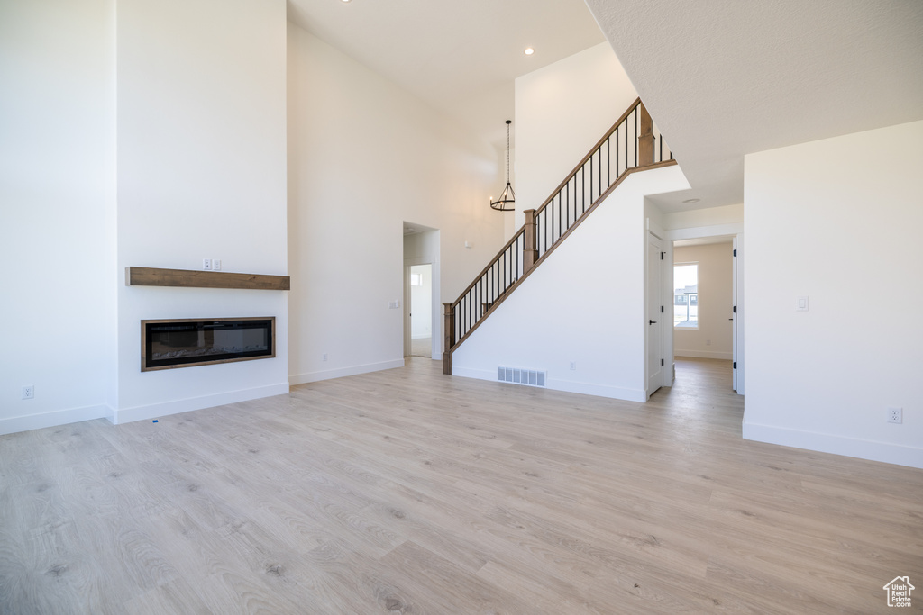 Unfurnished living room featuring stairway, light wood finished floors, a glass covered fireplace, a high ceiling, and recessed lighting