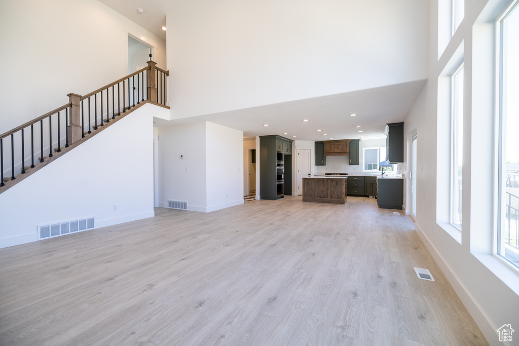 Unfurnished living room featuring a towering ceiling, light wood-style floors, stairway, and recessed lighting