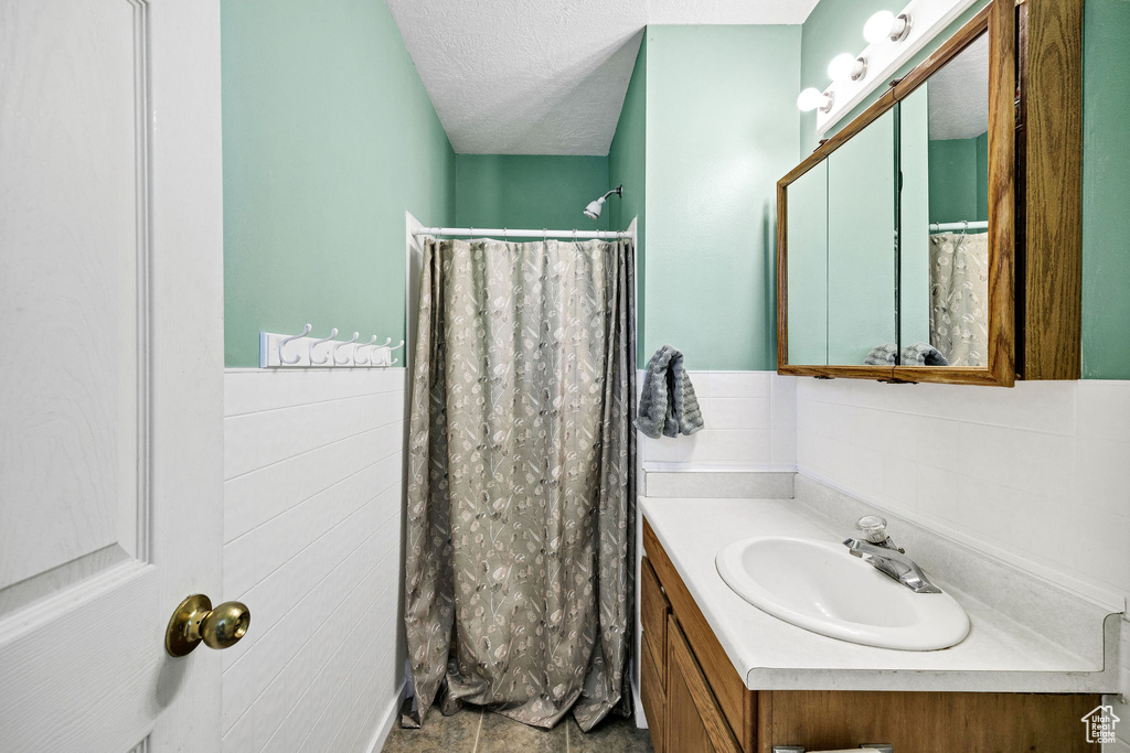 Bathroom with vanity, a wainscoted wall, a textured ceiling, curtained shower, and tile walls