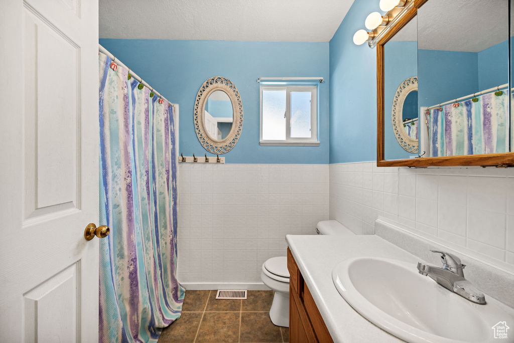 Bathroom featuring tile patterned flooring, tile walls, vanity, and a wainscoted wall