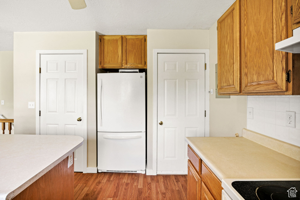 Kitchen featuring freestanding refrigerator, wood finished floors, light countertops, and brown cabinetry