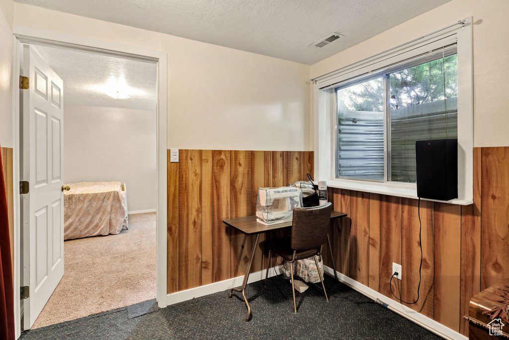 Office area featuring carpet flooring, wooden walls, a textured ceiling, and a wainscoted wall