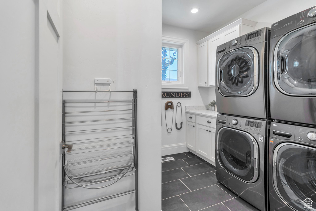 Washroom with cabinet space, independent washer and dryer, stacked washer and clothes dryer, dark tile patterned flooring, and recessed lighting