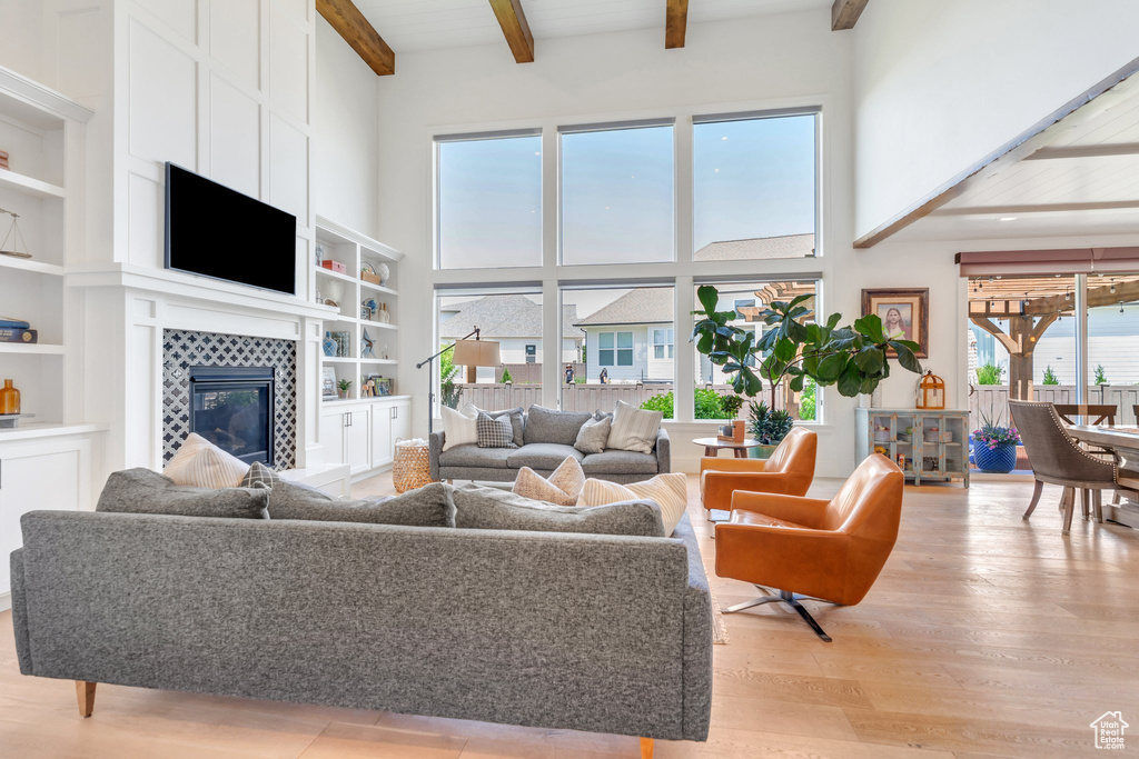 Living room featuring a high ceiling, light wood-style floors, beam ceiling, a tile fireplace, and built in shelves