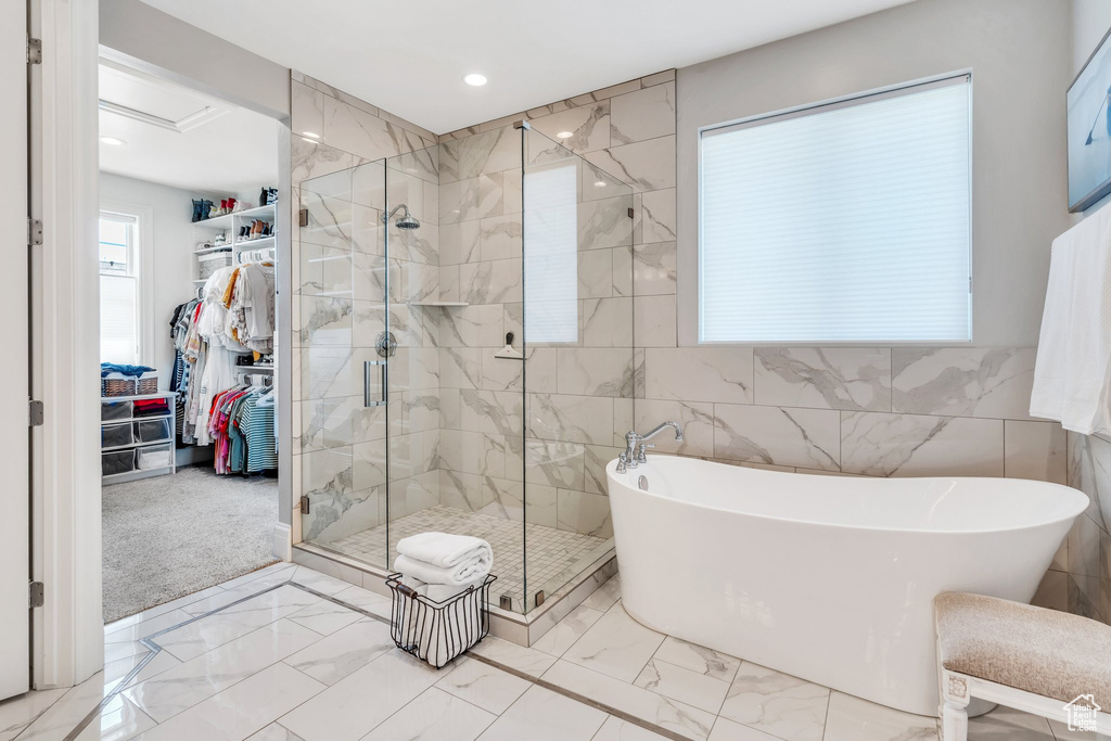 Full bathroom featuring marble look tiles, a soaking tub, a stall shower, a walk in closet, and recessed lighting