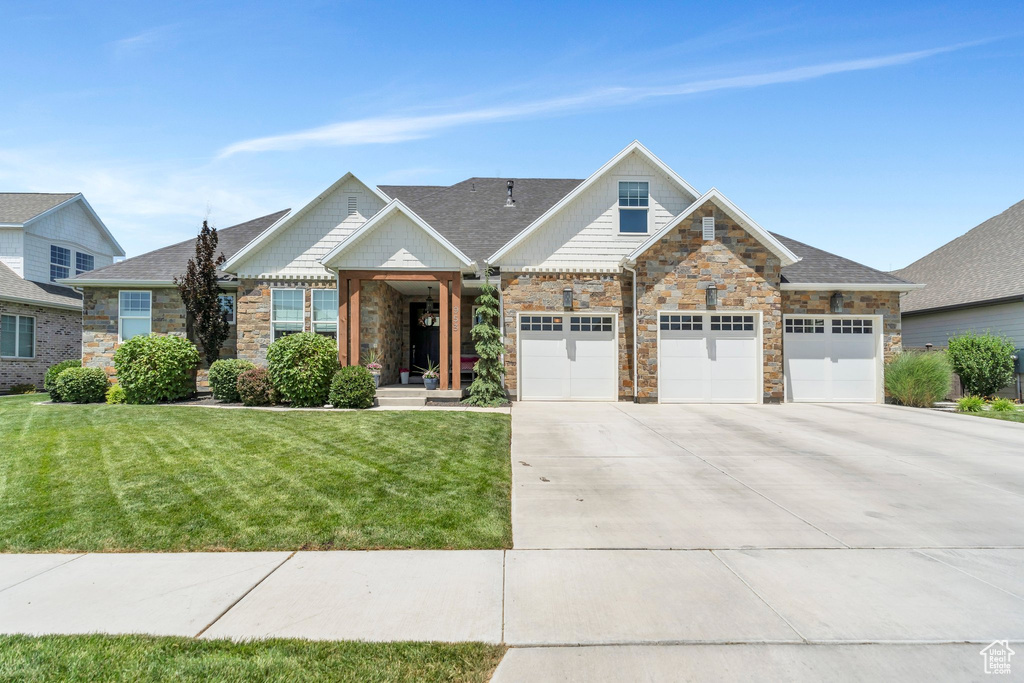 View of front facade featuring stone siding, driveway, a front lawn, and a garage