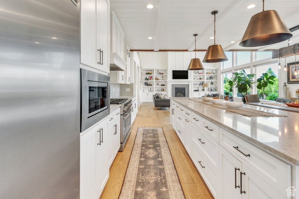 Kitchen with stainless steel appliances, open floor plan, light wood-style flooring, a fireplace, and white cabinetry