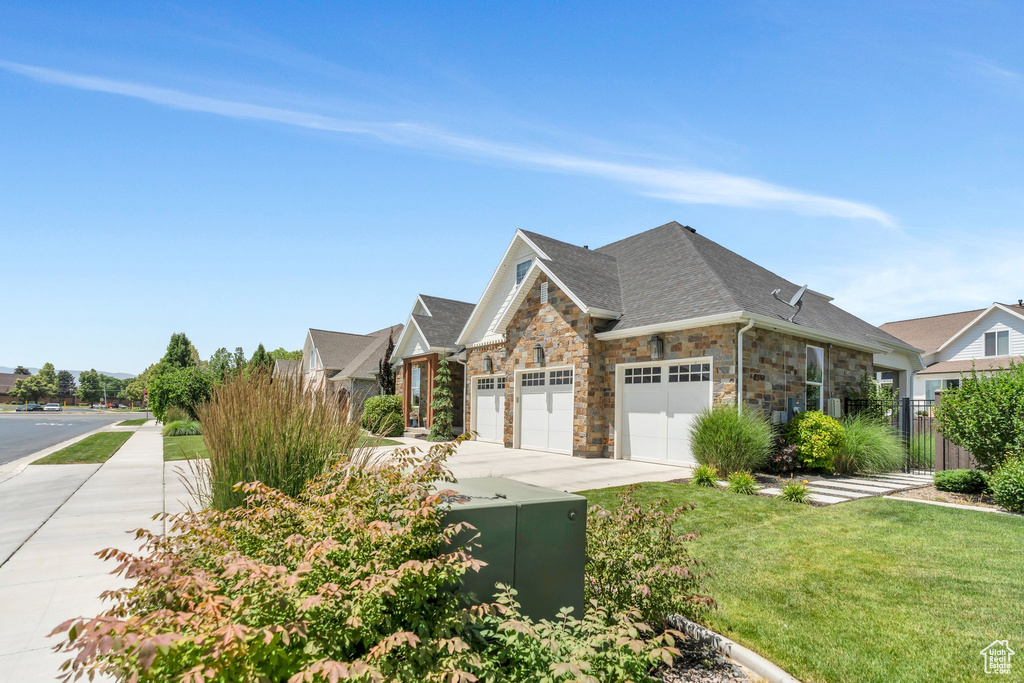 View of front facade featuring an attached garage, stone siding, concrete driveway, and roof with shingles