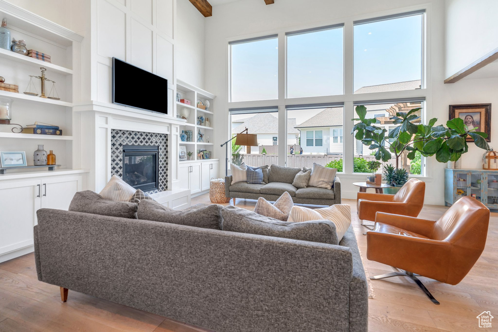 Living area with healthy amount of natural light, light wood-style flooring, a tile fireplace, a towering ceiling, and built in shelves