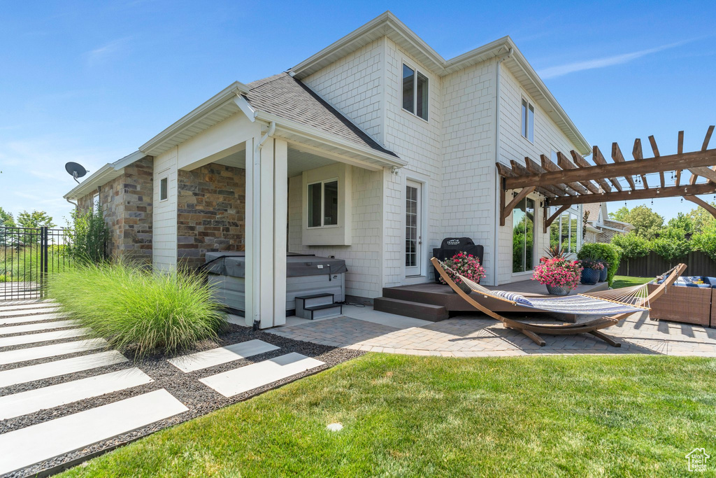Rear view of property with a hot tub, a patio, a pergola, and roof with shingles