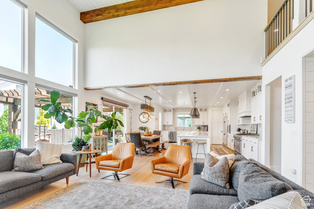 Living area with a high ceiling, light wood-style floors, beam ceiling, and a chandelier