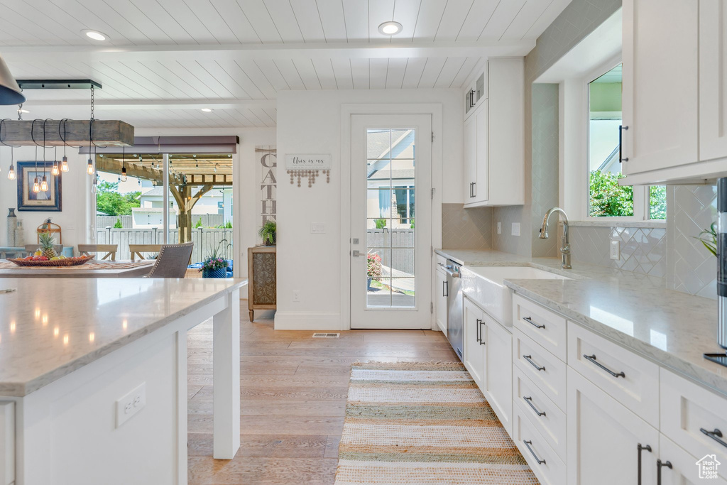 Kitchen featuring light wood-style flooring, tasteful backsplash, a wooden ceiling with exposed beams, white cabinetry, and stainless steel dishwasher