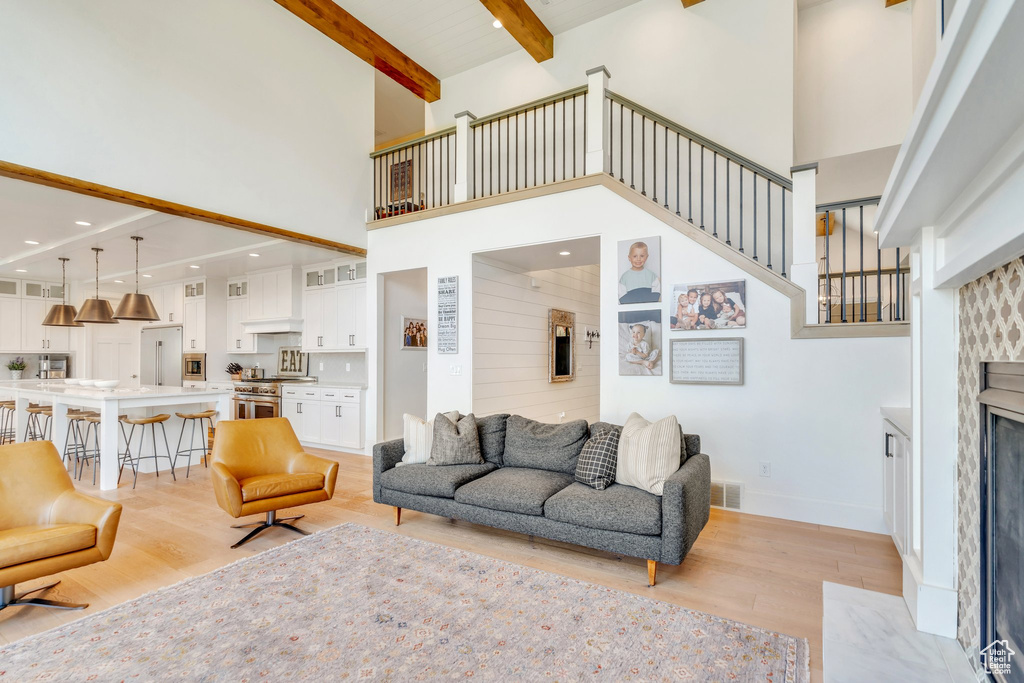 Living area with a towering ceiling, light wood-style floors, a premium fireplace, beamed ceiling, and stairs