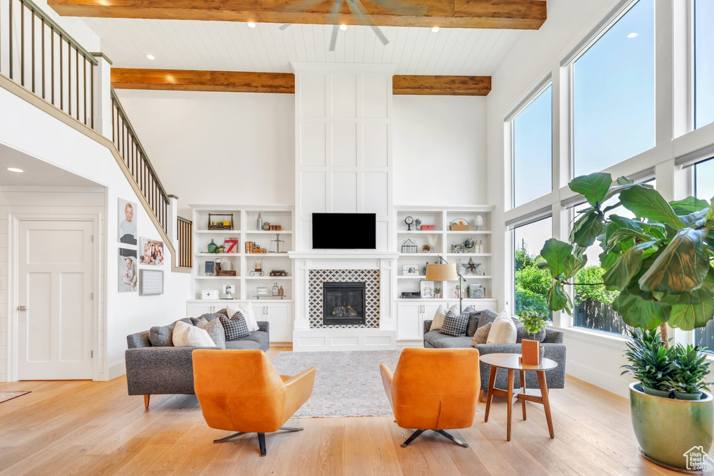 Living area featuring a towering ceiling, plenty of natural light, light wood-style floors, beam ceiling, and a tiled fireplace